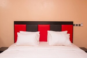 Habitación de hotel con una cama y cabecera roja, y ropa de cama blanca.