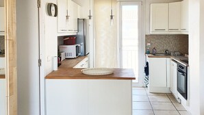 A modern kitchen with white cabinets, a wooden countertop, and a central island. There are pendant lights, a microwave, and a stove.