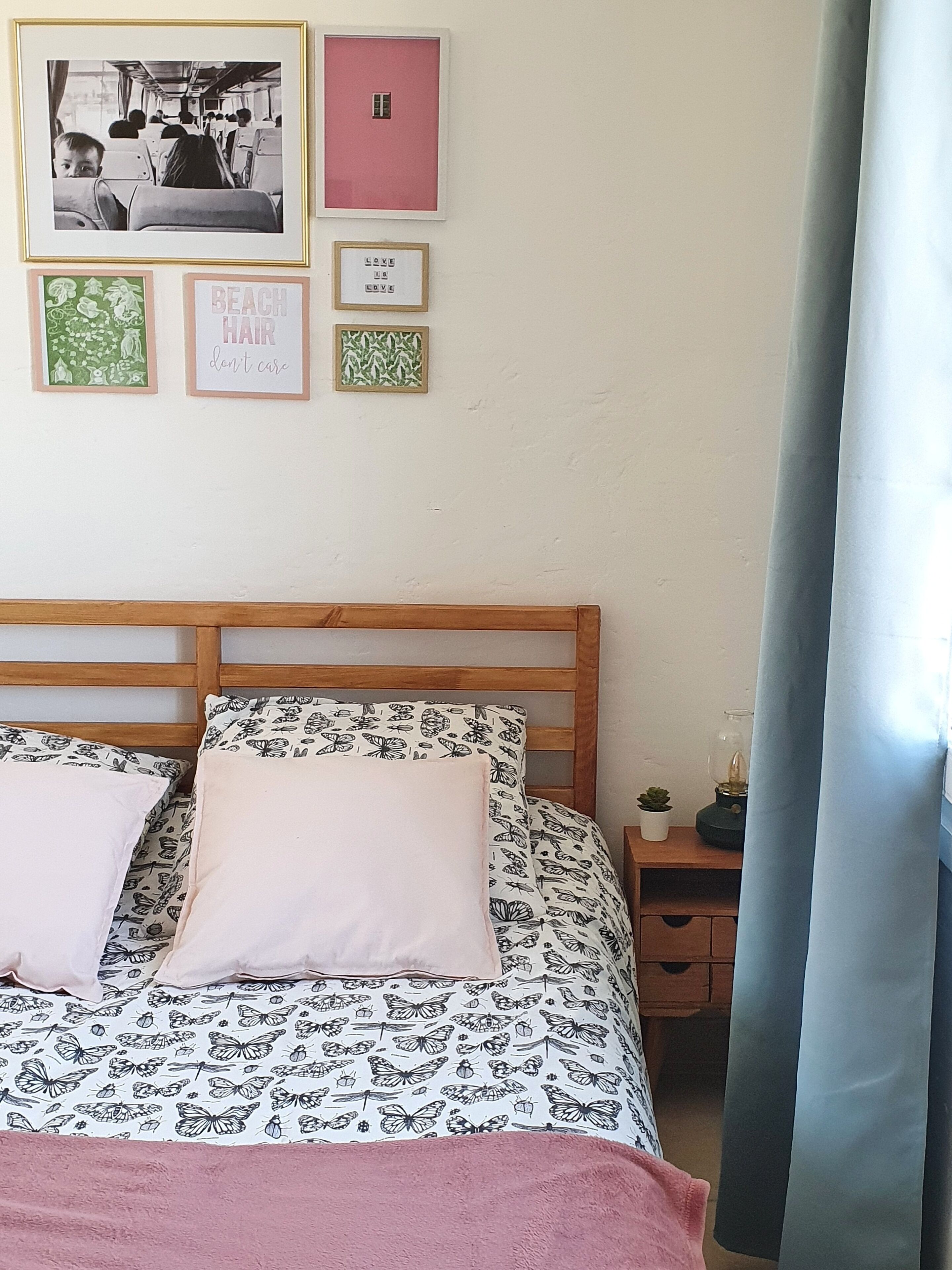 A bedroom with a wooden bed, two pillows, a nightstand with a lamp, and a wall with framed pictures.