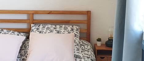 A bedroom with a wooden bed, two pillows, a nightstand with a lamp, and a wall with framed pictures.