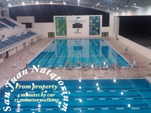Enjoy a swim in the San Juan Natatorium's indoor pool, featuring multiple lanes and a spectator area with seating.