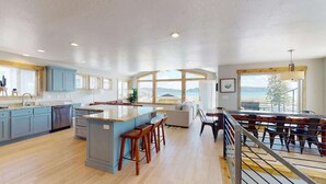 Une cuisine spacieuse dotée d’un grand îlot central, de tabourets de bar en bois et offrant une vue sur la mer grâce à de grandes fenêtres.