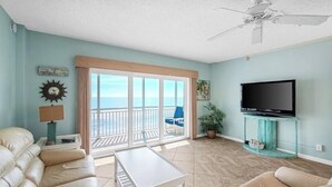A living room with a sofa, a coffee table, a TV on a stand, a ceiling fan, and a view of the ocean through large sliding doors. - Breathtaking Views from this 5th floor Ocean Front Condo  (Satellite Beach)