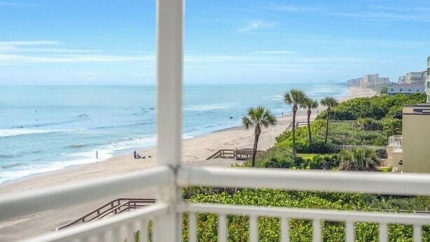 A beach view from a balcony with a railing, ocean, and buildings in the background. - Breathtaking Views from this 5th floor Ocean Front Condo  (Satellite Beach)