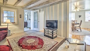 Ein Wohnzimmer mit Fernseher, einem roten Teppich, einer Holzkiste und einem durchgehenden Essbereich.