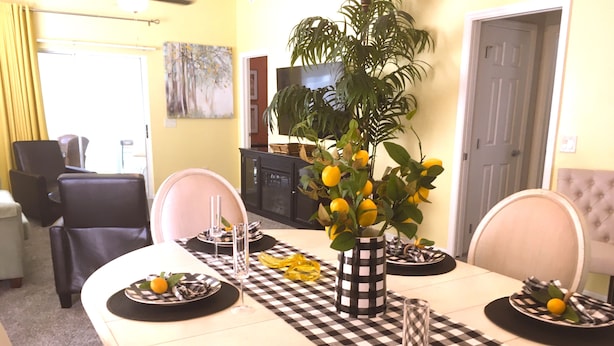 Un comedor con mantel a cuadros, un florero con limones y una planta en maceta.