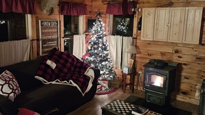 L’intérieur d’un chalet chaleureux, avec un plafond en bois, une cheminée, un sapin de Noël et un canapé recouvert d’une couverture.