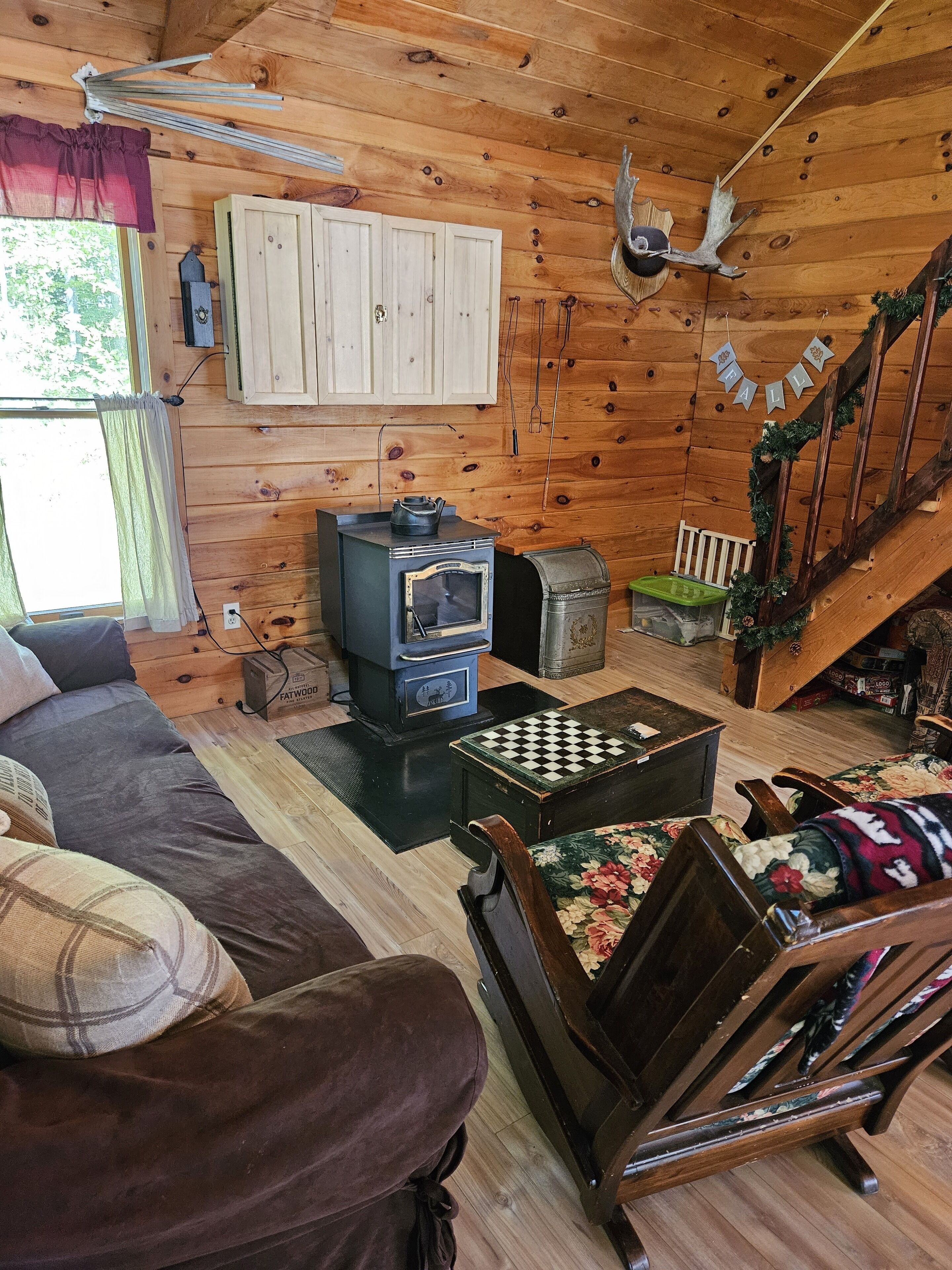 Interior acogedor de una cabaña con paredes y detalles de madera, chimenea, sofá, silla de madera y una escalera.