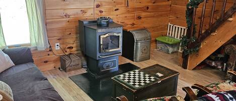 Interior acogedor de una cabaña con paredes y detalles de madera, chimenea, sofá, silla de madera y una escalera.