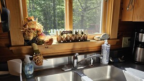 Une cuisine dotée d’un évier à deux bacs, de meubles en bois, d’une fenêtre donnant sur les arbres et d’un panneau décoratif posé sur le rebord de la fenêtre.