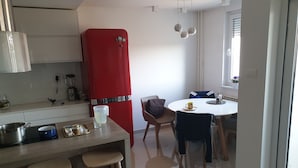 A modern kitchen with a red Bosch refrigerator, a wooden countertop, and a dining area with a white table and chairs. - Maleni stan (Zagreb)