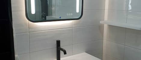 A bathroom with a white sink, black faucet, and a mirror with illuminated edges.