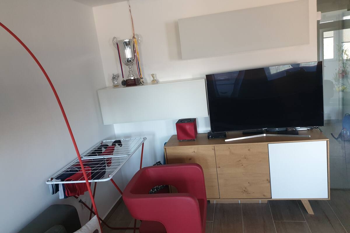 A modern living room with a flat-screen TV, a red chair, a small table, and a clothes drying rack.
