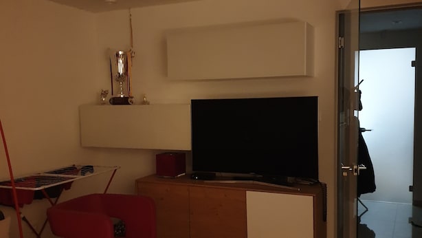 A living room with a TV, a red chair, a white table, and a glass door leading to another room. - Maleni stan (Zagreb)
