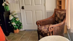 A room with a white door, a patterned rug, a white chair, and a wicker chair.