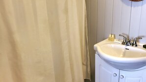 A bathroom with a white sink, a mirror with an ornate frame, a shower curtain, and a red towel on a chair.
