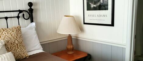 A hotel room with a bed, a nightstand with a lamp, a framed picture on the wall, and a door to the right.