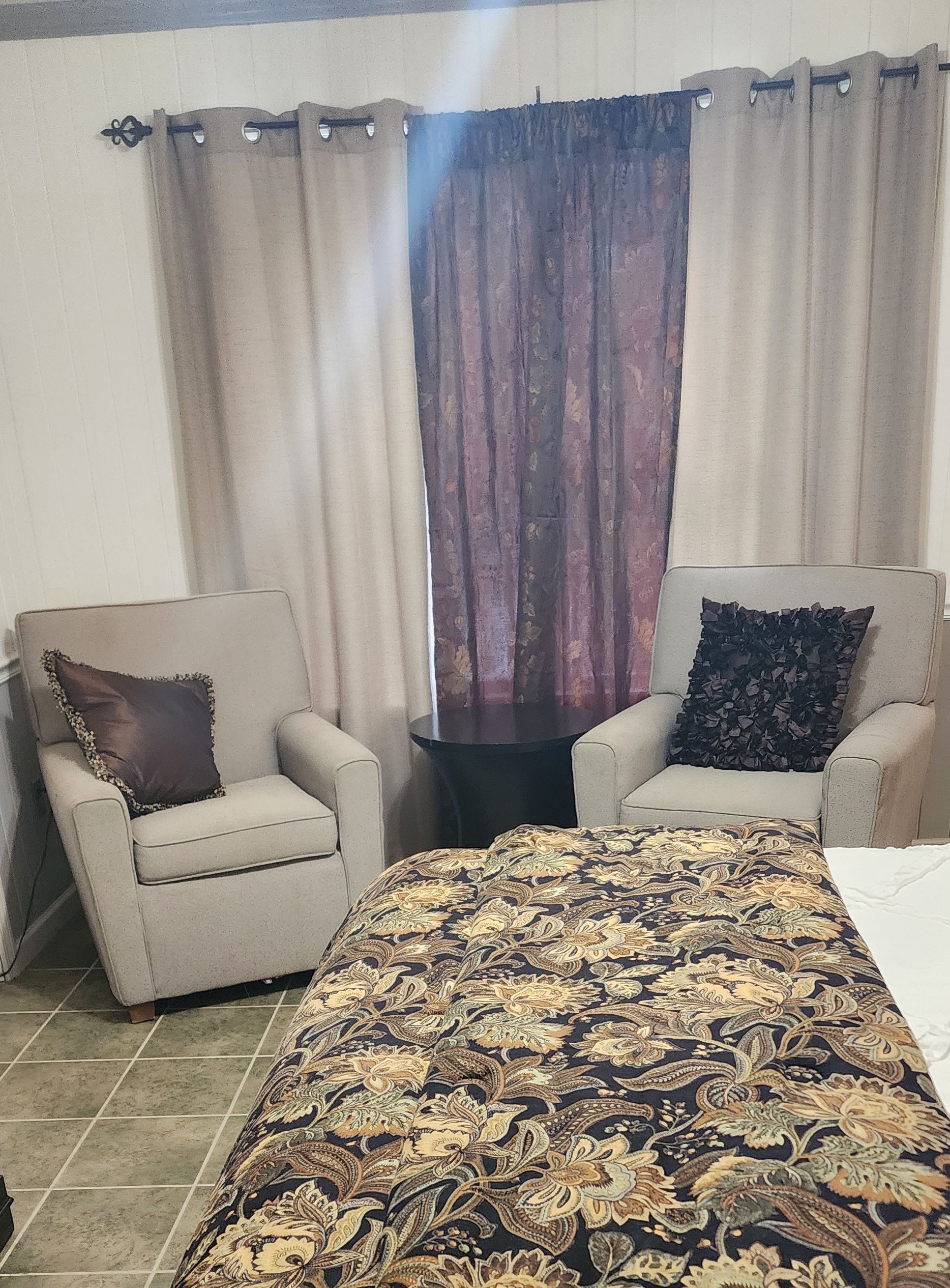 A room with two armchairs, a small table, and a bed with a patterned bedspread.
