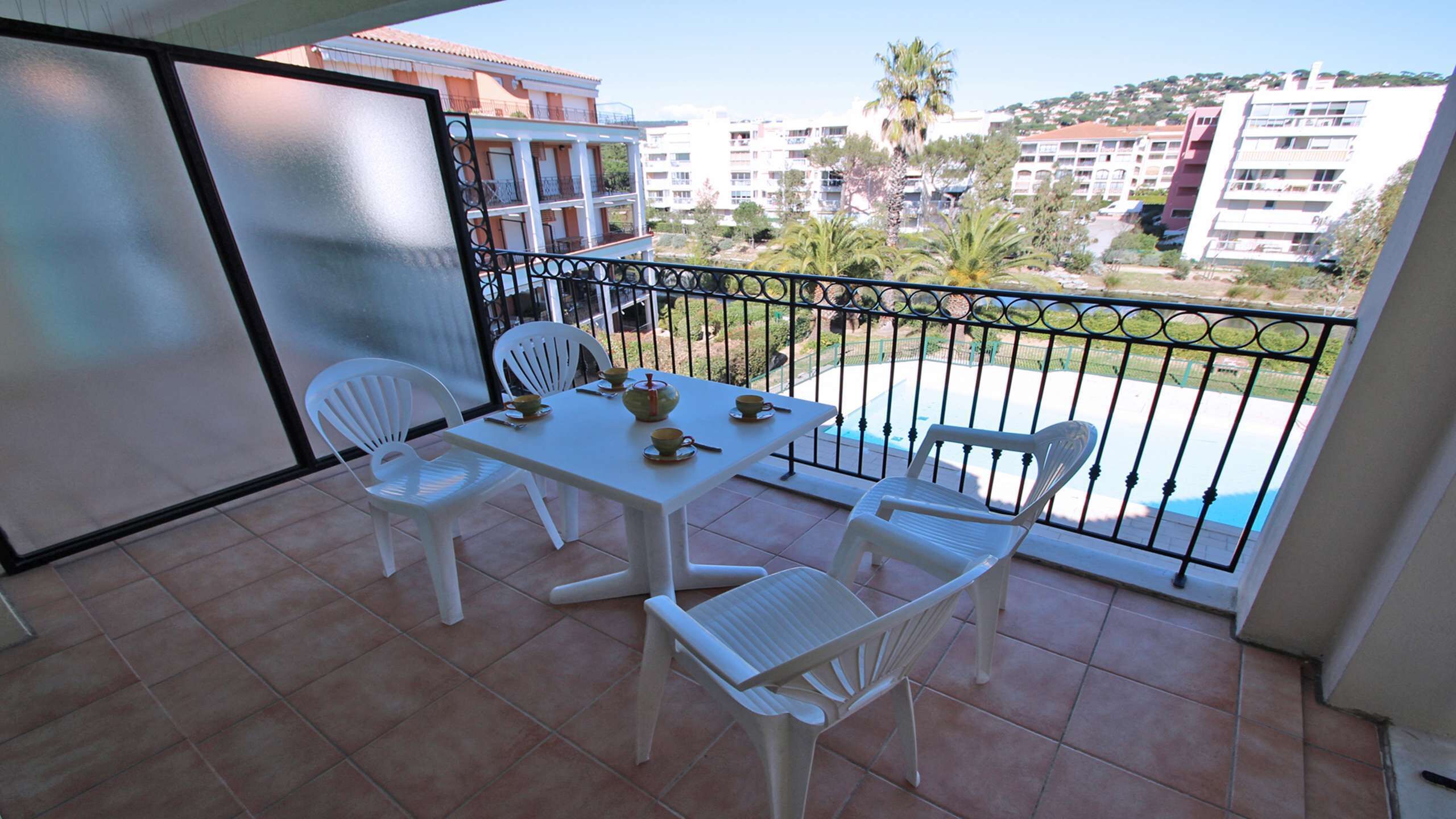 Un balcon avec une table et des chaises blanches, une piscine et des bâtiments en arrière-plan.