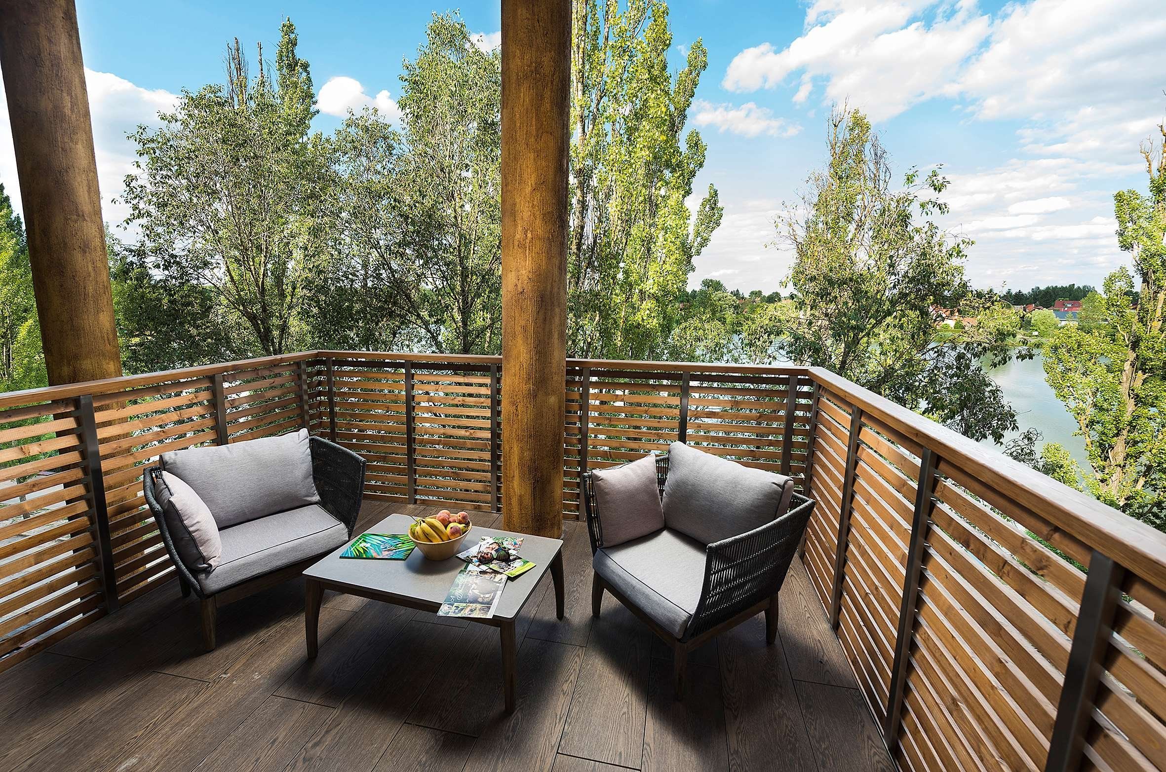 Un balcón con dos sillones acolchados, una mesa con frutero y vistas a un río y árboles.