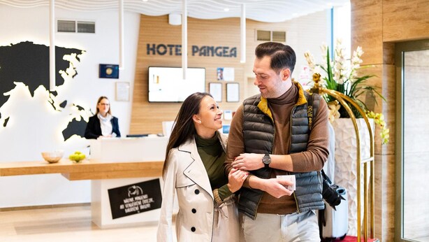 Zona de recepción de un hotel con mostrador de recepción, un mapa mundial decorativo y un cartel que dice 'HOTEL PANGEA'.