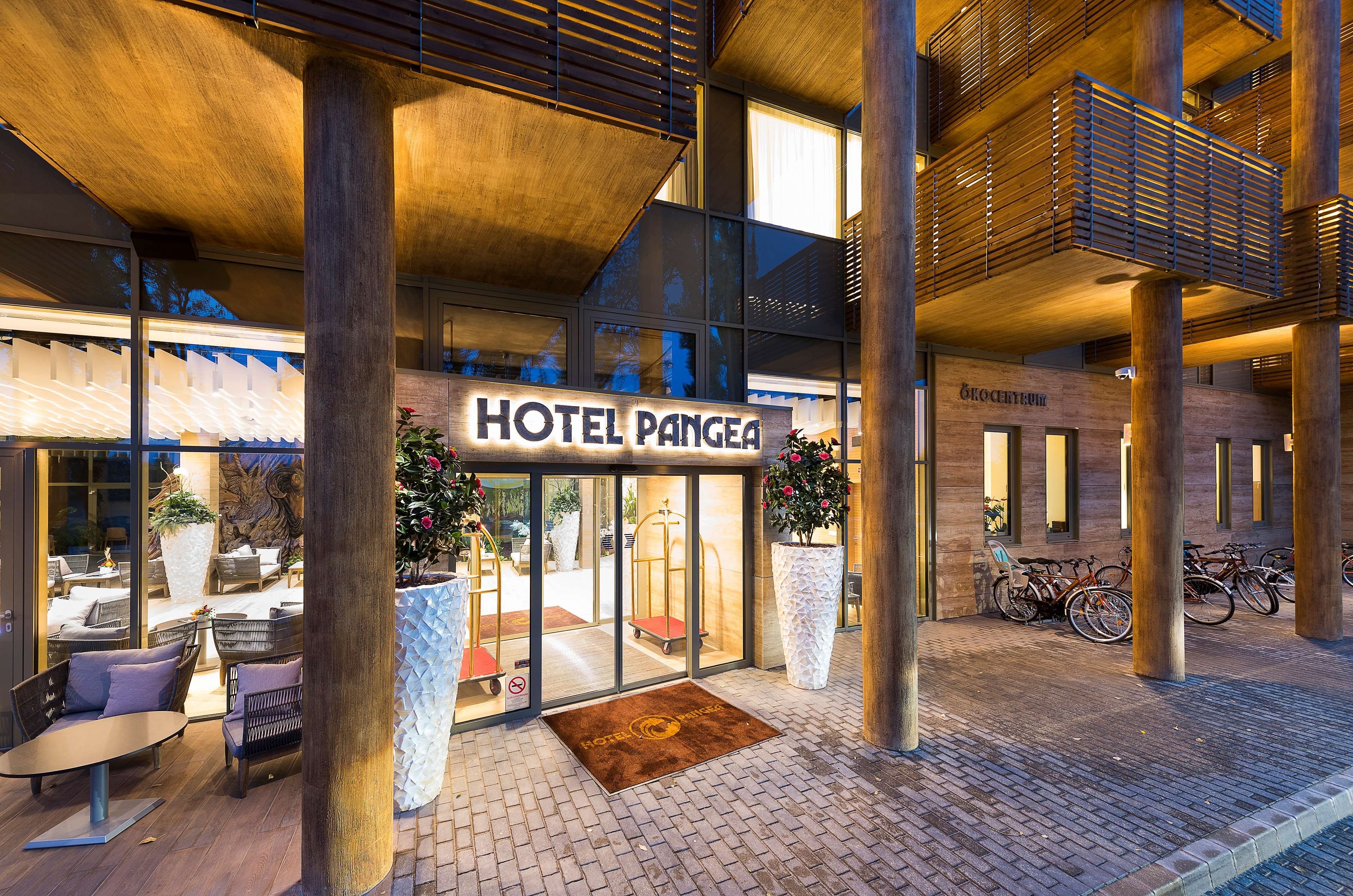 Entrada de hotel con un letrero que dice "HOTEL PANGEA", mesas al aire libre y zona de estacionamiento para bicicletas.