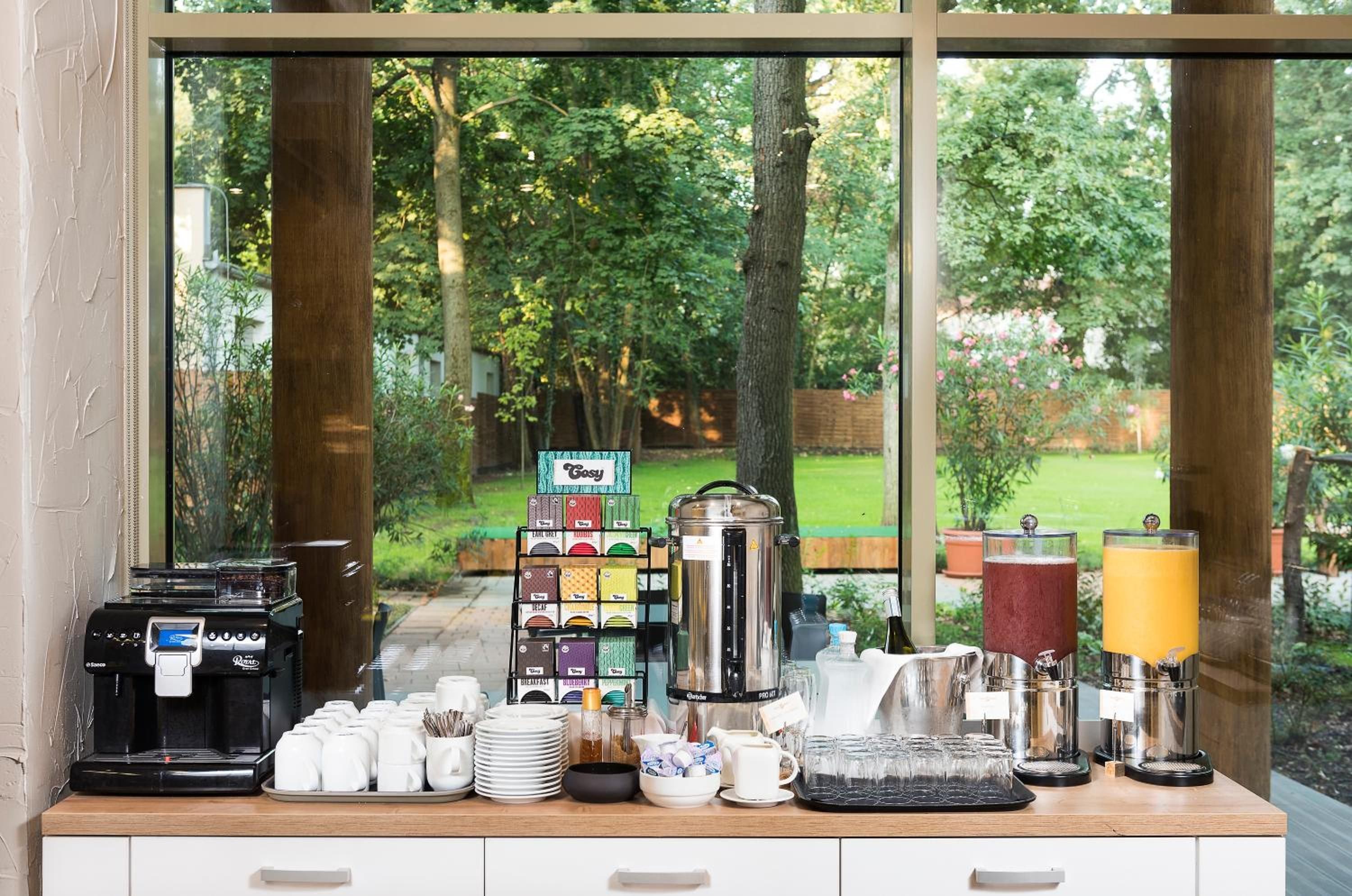 A breakfast bar with coffee machines, tea and juice dispensers, and a view of a garden.