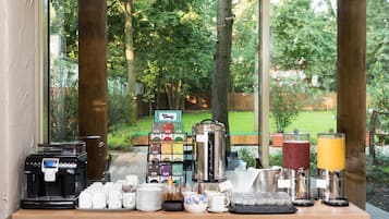 A breakfast bar with coffee machines, tea and juice dispensers, and a view of a garden.