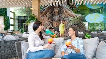 A lounge area with wicker furniture, a mural with a tree and human figures, and a glass table with drinks.