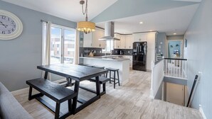A modern kitchen with a central island, a dining area with a wooden table, and a staircase leading to an upper level. - Renovated with Backyard Oasis! Quick Walk to Town & Beach. 4 BRs. Sleeps 10 (Sea Isle City)