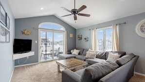 A living room with a grey sofa set, a wooden coffee table, a flat-screen TV on a white shelf, and a ceiling fan. - Renovated with Backyard Oasis! Quick Walk to Town & Beach. 4 BRs. Sleeps 10 (Sea Isle City)