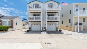 A two-story residential building with a central garage, a balcony on the upper floor, and a flag on the right side. - Renovated with Backyard Oasis! Quick Walk to Town & Beach. 4 BRs. Sleeps 10 (Sea Isle City)