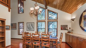 A dining area with a wooden table and chairs, large windows, and a chandelier. - MtnScape_Views, EV Charger, GameRoom, Pool Table /PingPong, Arcade +HOA Amenities (Gym/Sauna/Pool) (Truckee)