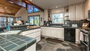 A modern kitchen with white cabinets, a black dishwasher, and a stone backsplash. - MtnScape_Views, EV Charger, GameRoom, Pool Table /PingPong, Arcade +HOA Amenities (Gym/Sauna/Pool) (Truckee)
