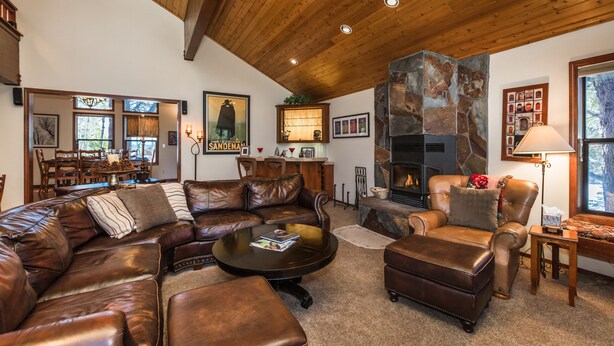 A cozy living room with a leather sectional sofa, a fireplace, and a dining area visible through a glass door. - MtnScape_Views, EV Charger, GameRoom, Pool Table /PingPong, Arcade +HOA Amenities (Gym/Sauna/Pool) (Truckee)