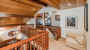 A spacious loft with a high ceiling, wooden beams, a dining area with a chandelier, a staircase, and a beige sofa. - MtnScape_Views, EV Charger, GameRoom, Pool Table /PingPong, Arcade +HOA Amenities (Gym/Sauna/Pool) (Truckee)