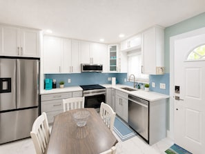 A modern kitchen with white cabinets, stainless steel appliances, and a blue accent wall.