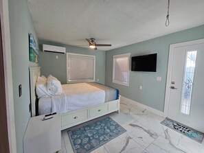 Camera da letto con un letto, ventilatore a soffitto, condizionatore e televisore appeso al muro.