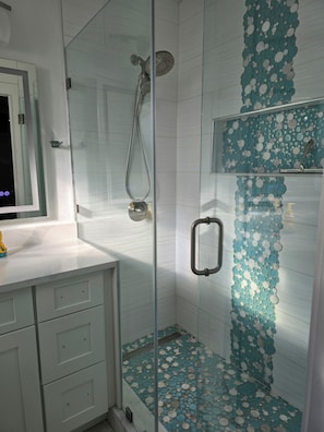 A glass-enclosed shower with a rain showerhead, a white tiled wall, and a decorative blue and white tile pattern on the floor.