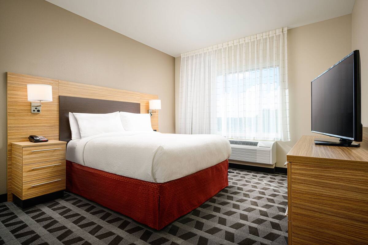 Ein Hotelzimmer mit Bett, Nachttischen, einem Fernseher und einem Fenster mit Vorhängen.