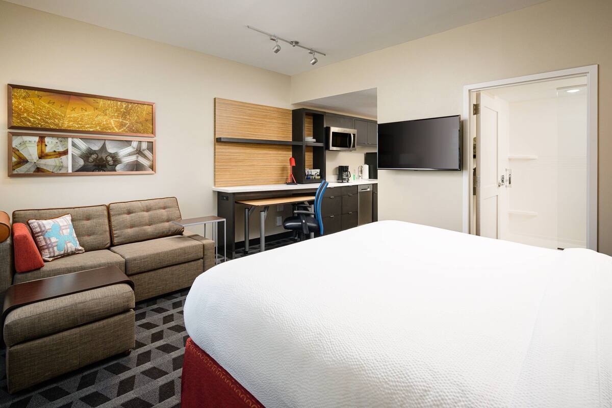 Ein Hotelzimmer mit einem Bett, einer Couch, einem Schreibtisch mit Computer, einem Fernseher und einer Mikrowelle.