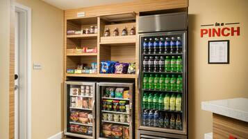 A kitchenette with a refrigerator stocked with beverages, a freezer, and shelves with snacks and condiments.
