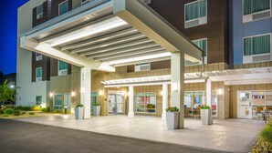 A modern hotel entrance with a covered walkway, large windows, and outdoor seating area.