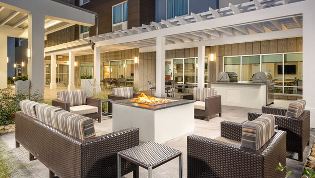 An outdoor patio area with wicker furniture, a central fire feature, and a covered seating area.