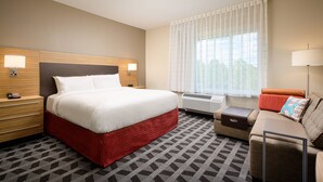 A hotel room with a large bed, a sofa, a desk, and a window with curtains.