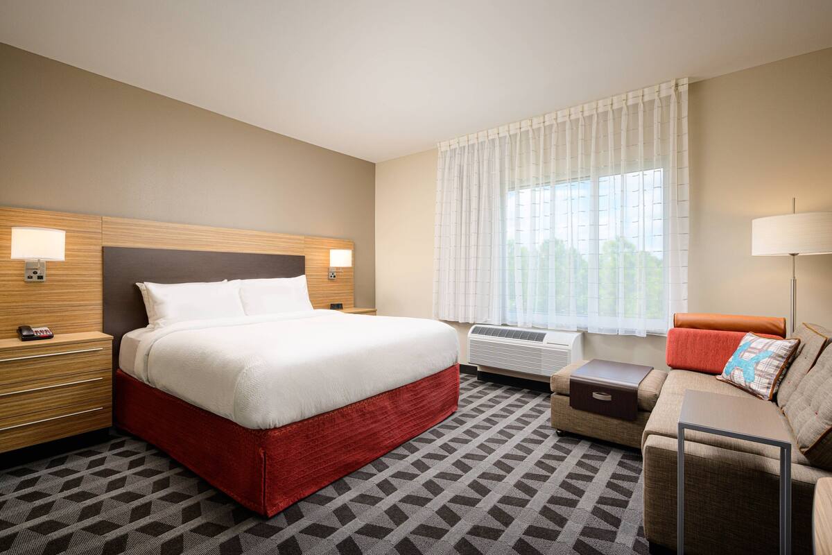 Ein Hotelzimmer mit einem großen Bett, einer Couch, einem Schreibtisch und einem Vorhangfenster.