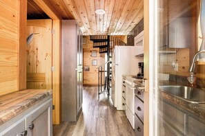 A narrow kitchen with wooden walls, a white stove, and a stainless steel sink.