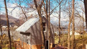 A wooden cabin with a metal roof, surrounded by trees and a clear sky. - Blue Heron Treehouse - Private Hot Tub (Guild)
