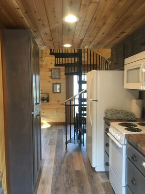 A kitchen with wooden flooring, a white refrigerator, a stove, and a black spiral staircase leading to an upper level.