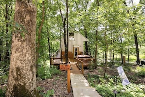 A wooden cabin with a deck and a sign reading 'BLUE HERON' in a forested area.